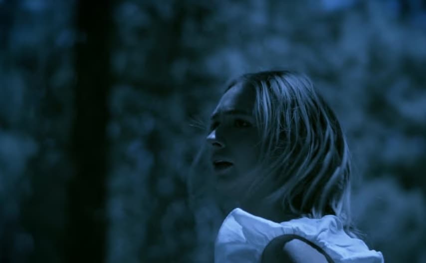 A still from The Crest: a young woman in blue night light looking over her shoulder